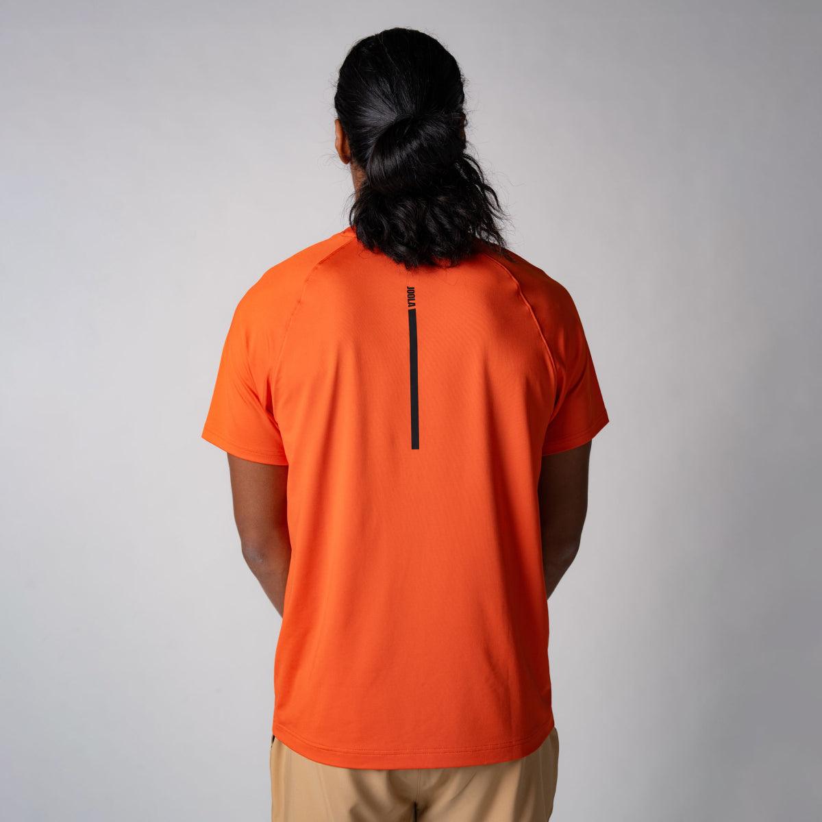 Mann von hinten mit orangefarbenem T-Shirt und kurzem schwarzen Aufdruck auf dem Rücken vor neutralem Hintergrund.