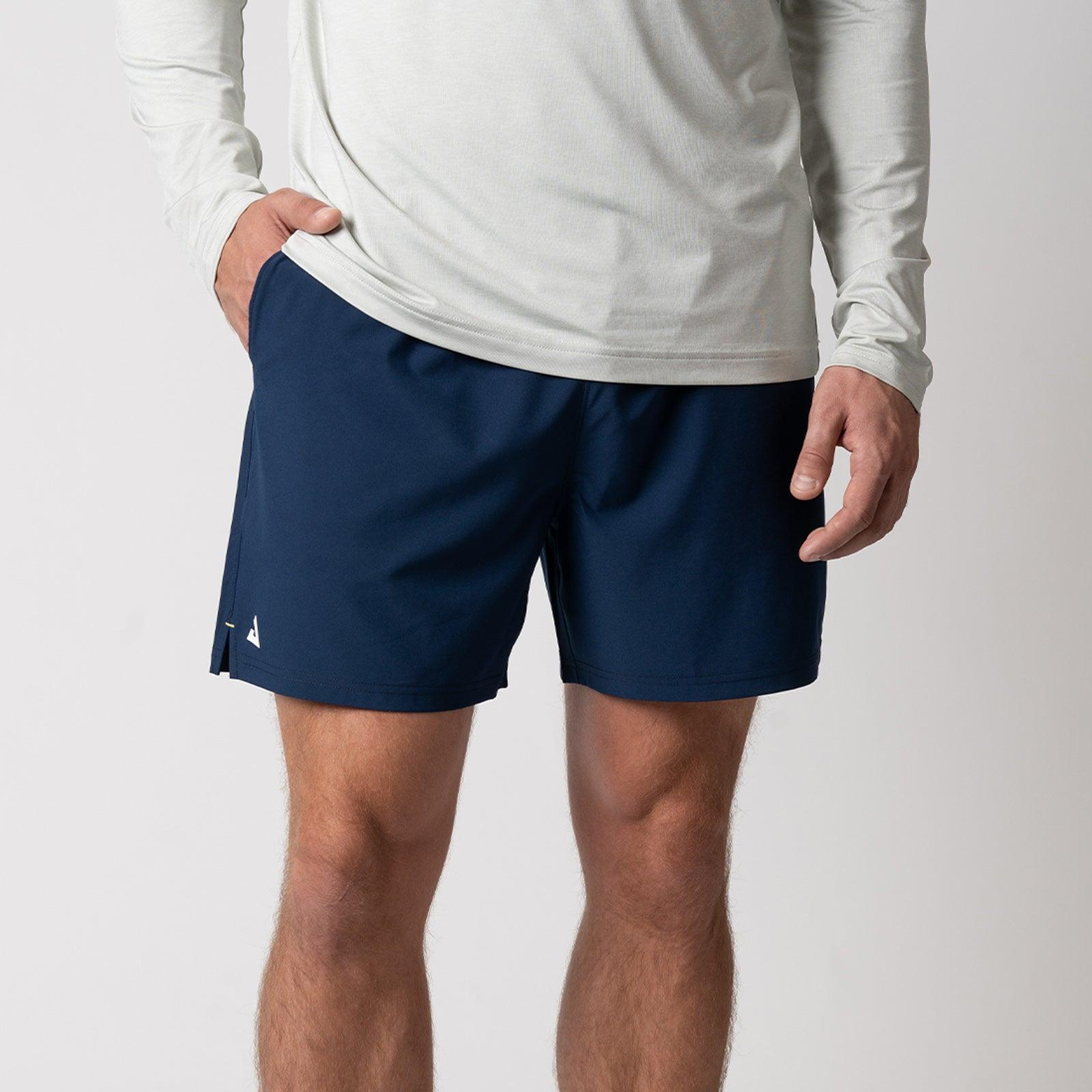 Mann trägt navyblaue Sportshorts und hellgraues Langarmshirt, Vorderansicht, Ausschnitt bis zur Hüfte.
