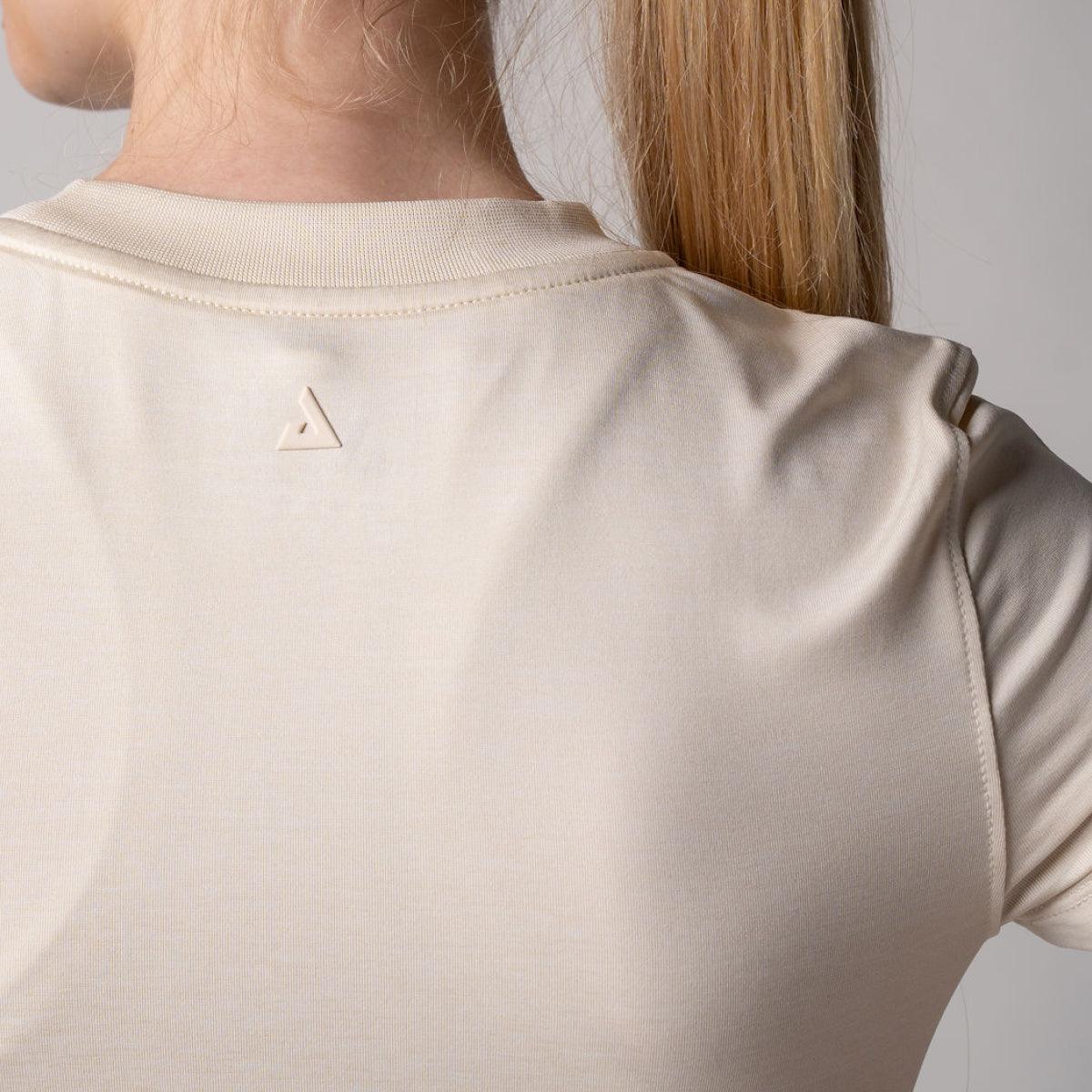 Beige T-Shirt-Rücken mit kleinem dreieckigem Logo unterhalb des Kragens.