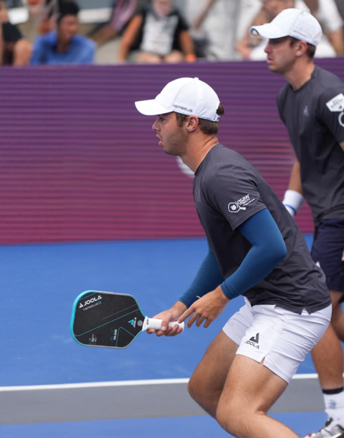 Zwei Männer in Sportkleidung spielen Pickleball, einer hält einen schwarzen JOOLA-Pickleball-Schläger.